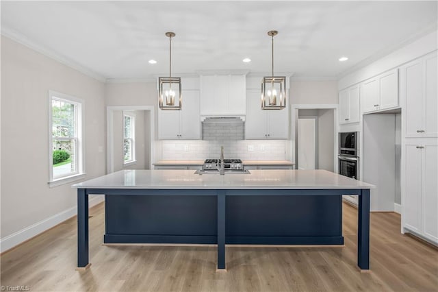 kitchen with a kitchen island with sink, sink, decorative light fixtures, and white cabinetry