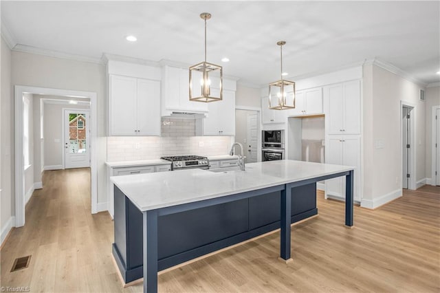 kitchen with an island with sink, sink, white cabinets, and decorative light fixtures