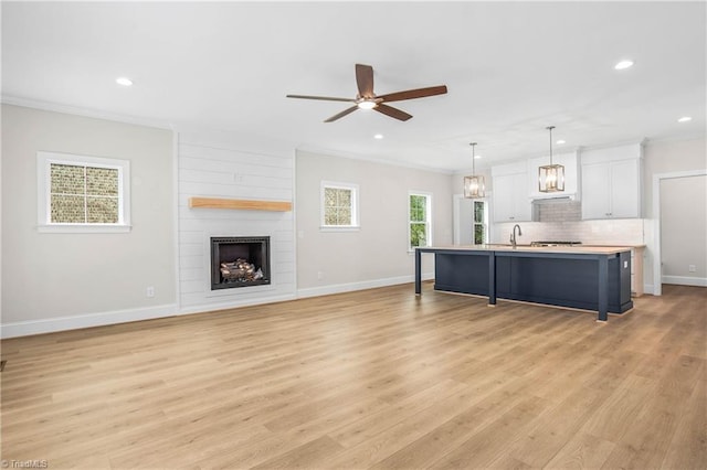 living room featuring light hardwood / wood-style flooring, ornamental molding, a large fireplace, and ceiling fan