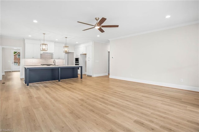 kitchen with crown molding, a kitchen island with sink, decorative backsplash, white cabinets, and decorative light fixtures