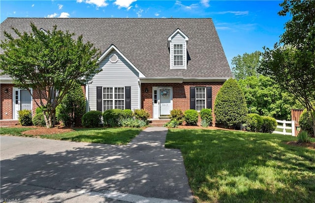 new england style home featuring brick siding, a front lawn, and roof with shingles