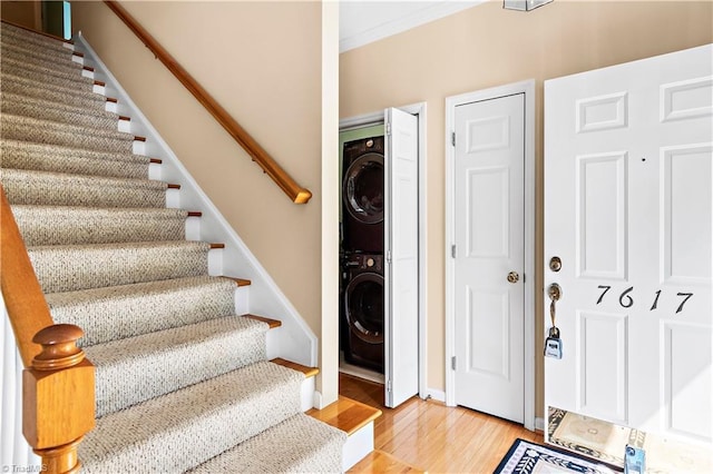 staircase featuring baseboards, stacked washer / drying machine, and wood finished floors