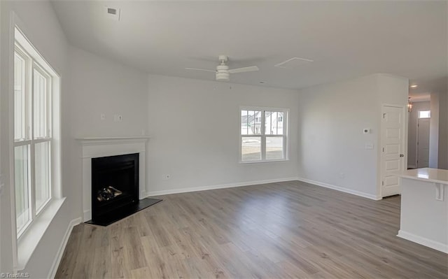 unfurnished living room featuring a fireplace with raised hearth, ceiling fan, wood finished floors, and baseboards