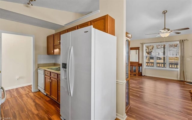 kitchen featuring brown cabinets, light countertops, decorative backsplash, wood finished floors, and white appliances