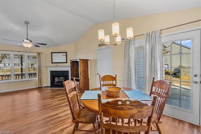 dining room with a wealth of natural light, light wood-type flooring, vaulted ceiling, and a fireplace with flush hearth