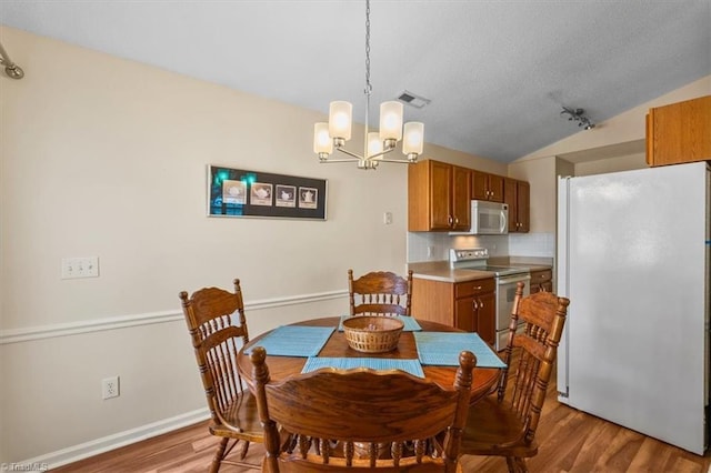 dining space featuring light wood finished floors, baseboards, visible vents, lofted ceiling, and a chandelier