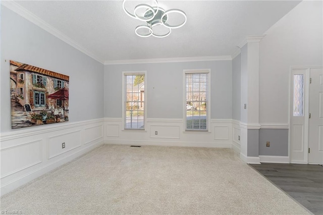 carpeted spare room featuring wainscoting, crown molding, and an inviting chandelier