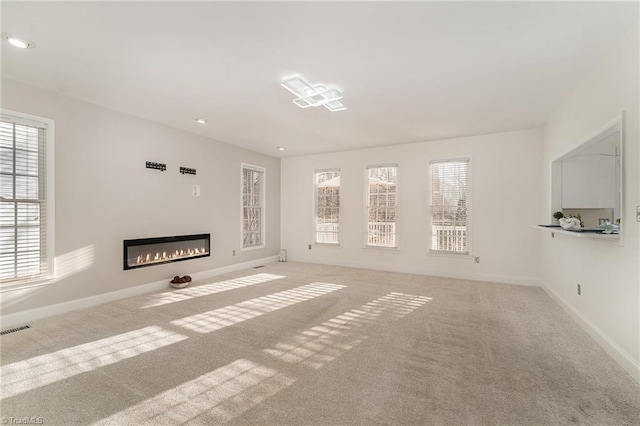 unfurnished living room with carpet flooring, a glass covered fireplace, visible vents, and baseboards