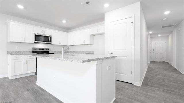 kitchen with white cabinets, stainless steel appliances, sink, light wood-type flooring, and a center island with sink