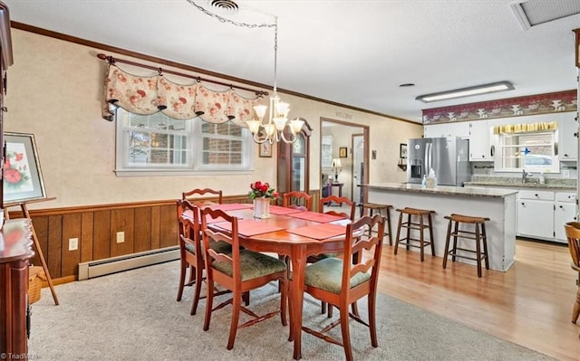 dining area featuring sink, crown molding, baseboard heating, light hardwood / wood-style floors, and a chandelier