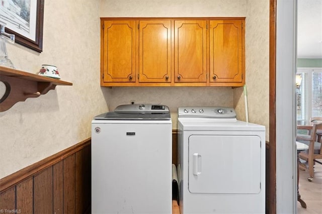 clothes washing area with wooden walls, washer and clothes dryer, and cabinets