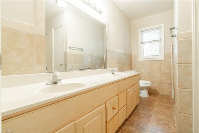 bathroom with tile walls, toilet, vanity with extensive cabinet space, double sink, and tile floors