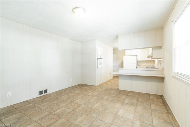 interior space featuring a kitchen bar, white cabinets, white appliances, and light tile floors