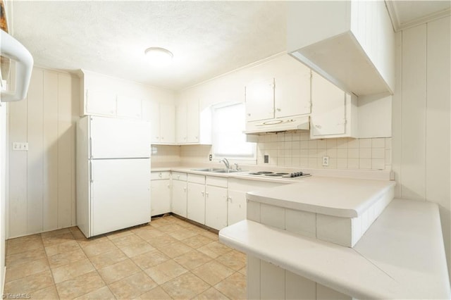 kitchen with custom exhaust hood, white fridge, white cabinets, sink, and light tile flooring