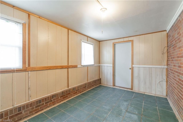 unfurnished room featuring brick wall, wood walls, dark tile floors, and ornamental molding