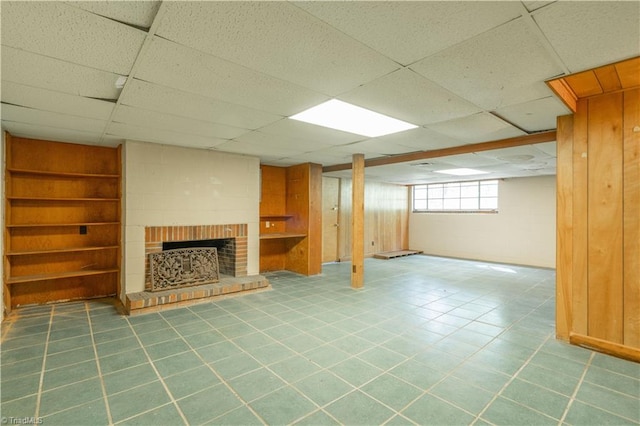 basement featuring built in shelves, tile floors, a paneled ceiling, and a brick fireplace