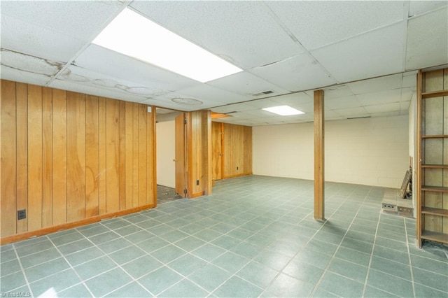 basement with tile flooring, a drop ceiling, and wooden walls