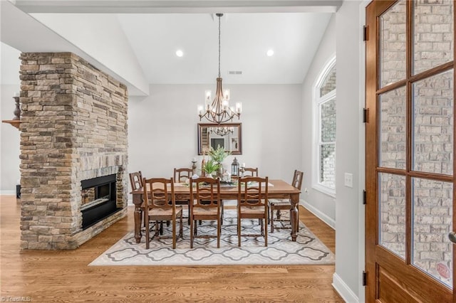 dining space with a stone fireplace, vaulted ceiling, light hardwood / wood-style floors, and a chandelier