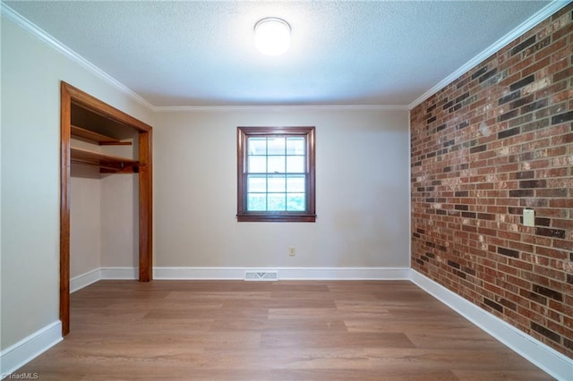 unfurnished bedroom featuring ornamental molding, light wood-type flooring, a closet, and brick wall