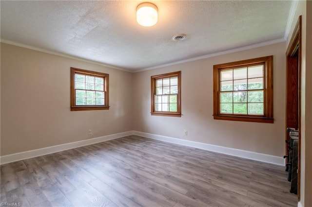 empty room with ornamental molding, a textured ceiling, plenty of natural light, and hardwood / wood-style floors