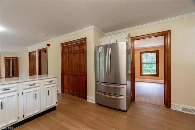 kitchen with white cabinets, light hardwood / wood-style flooring, stainless steel fridge, and ornamental molding