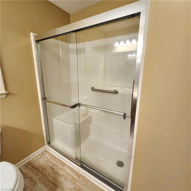 bathroom with an enclosed shower, wood-type flooring, a textured ceiling, and toilet