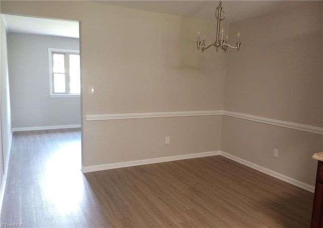 spare room with a notable chandelier and dark hardwood / wood-style flooring