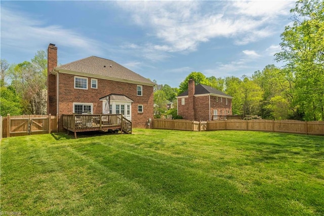 back of house featuring a chimney, a wooden deck, a yard, and a fenced backyard