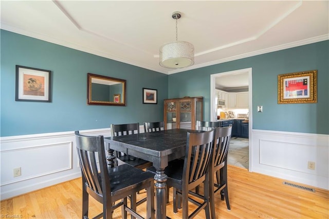 dining space with visible vents, light wood-style floors, a decorative wall, crown molding, and wainscoting