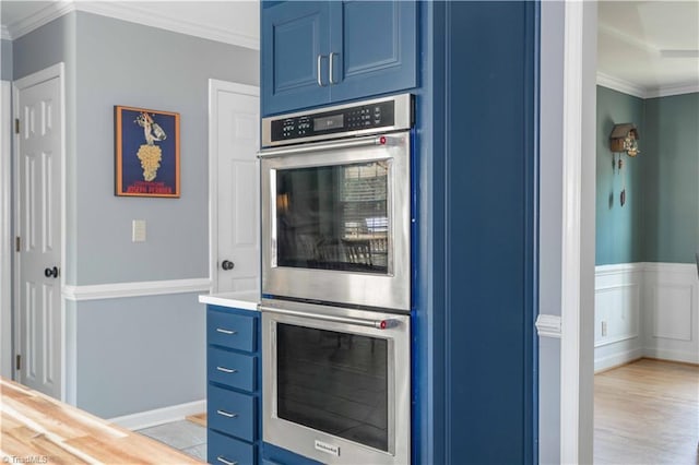 kitchen featuring double oven, light countertops, ornamental molding, light wood-style floors, and blue cabinetry