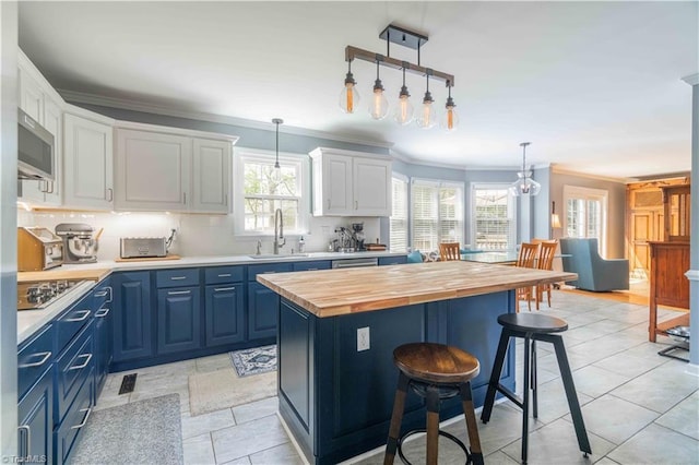 kitchen with a sink, white cabinets, butcher block counters, blue cabinetry, and ornamental molding