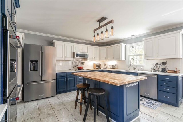 kitchen featuring wooden counters, stainless steel appliances, ornamental molding, a sink, and blue cabinetry