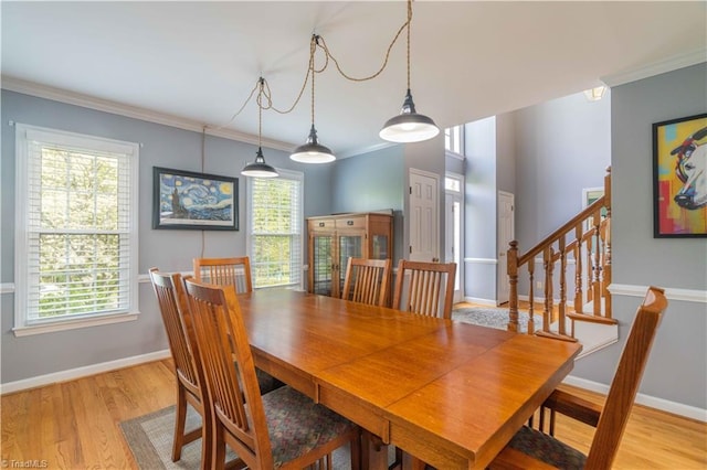 dining space with light wood-type flooring, crown molding, baseboards, and stairway
