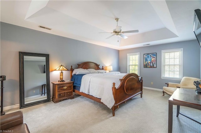 bedroom with baseboards, visible vents, light colored carpet, a ceiling fan, and a raised ceiling