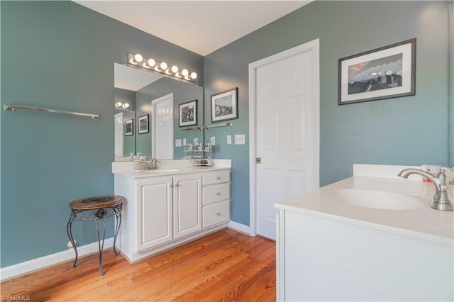 bathroom featuring two vanities, wood finished floors, baseboards, and a sink