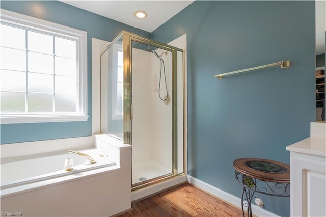 bathroom featuring baseboards, a bath, a stall shower, and wood finished floors