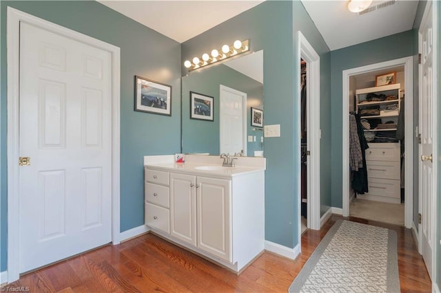 full bath featuring wood finished floors, visible vents, vanity, and a walk in closet