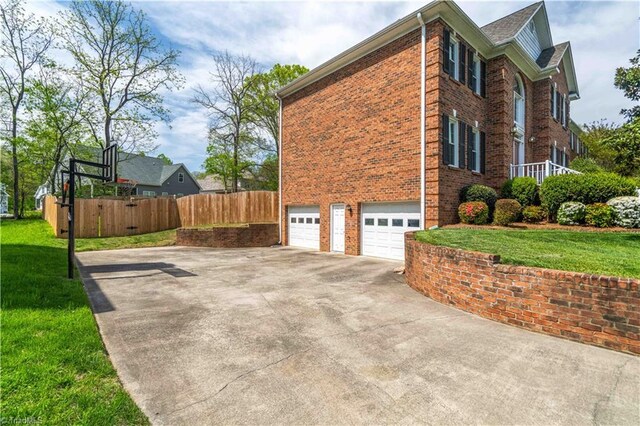view of side of property with driveway, fence, a garage, brick siding, and a lawn