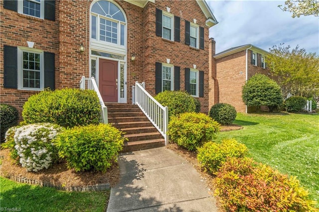 view of exterior entry featuring brick siding and a lawn