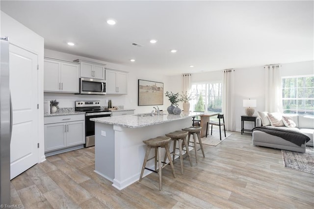 kitchen with light stone countertops, light wood-type flooring, a breakfast bar, stainless steel appliances, and an island with sink