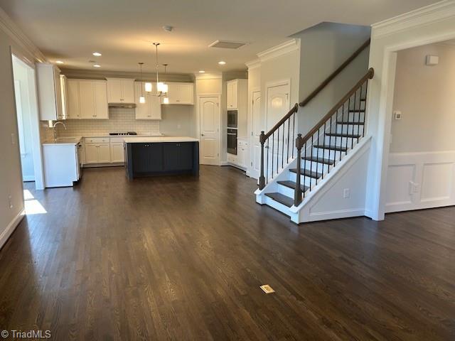 kitchen with pendant lighting, white cabinetry, sink, ornamental molding, and a center island