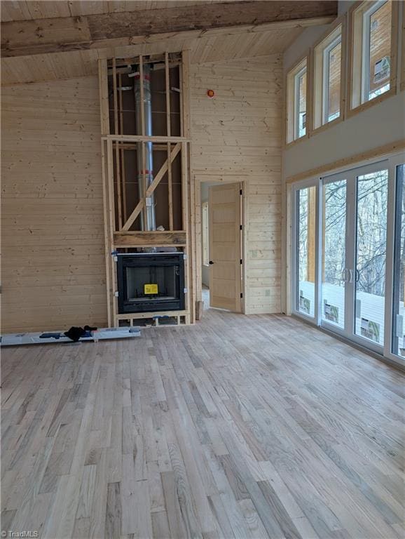 unfurnished living room featuring a towering ceiling, wood walls, wood finished floors, and beam ceiling