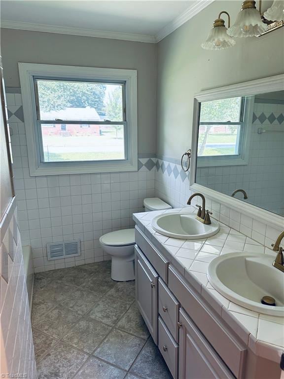 bathroom featuring dual bowl vanity, tile patterned floors, tile walls, crown molding, and toilet