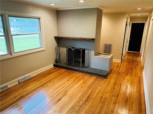 unfurnished living room with a fireplace, crown molding, brick wall, and wood-type flooring