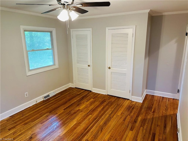 unfurnished bedroom featuring hardwood / wood-style floors, two closets, ornamental molding, and ceiling fan