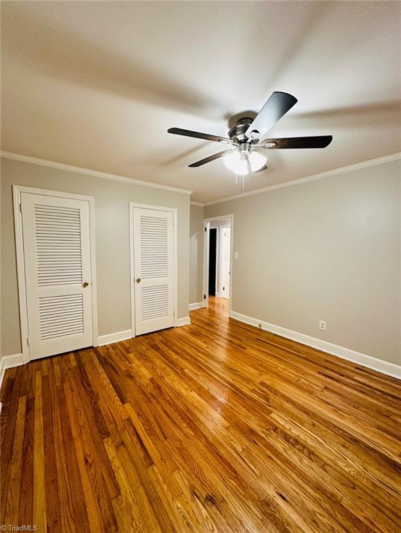 702 Trail One, Burlington, NC 27215 - unfurnished bedroom with crown molding, baseboards, wood finished floors, multiple closets, and ceiling fan