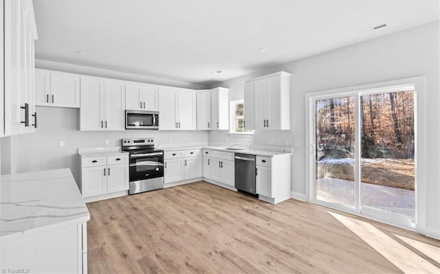 kitchen with a wealth of natural light, stainless steel appliances, white cabinetry, and light stone counters