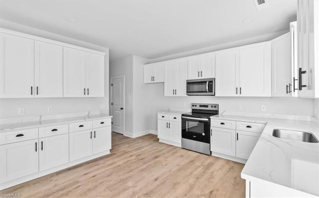 kitchen featuring stainless steel appliances, white cabinets, light wood-type flooring, and light stone counters