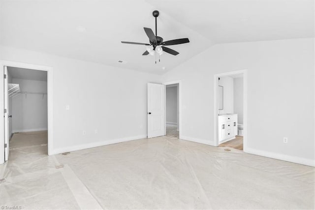 unfurnished bedroom featuring ensuite bathroom, vaulted ceiling, a spacious closet, ceiling fan, and a closet