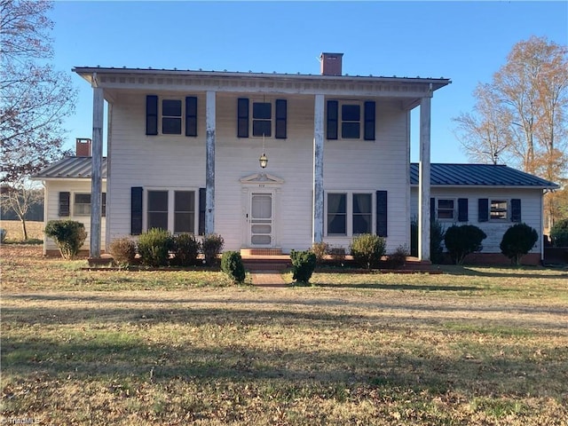 neoclassical / greek revival house with a chimney, a front lawn, and metal roof